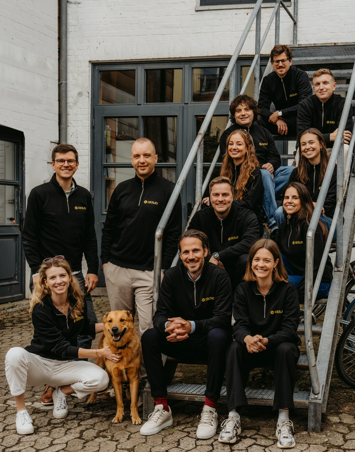 Das Team des AI Club auf einer Außentreppe, vorne der Bürohund Chapito