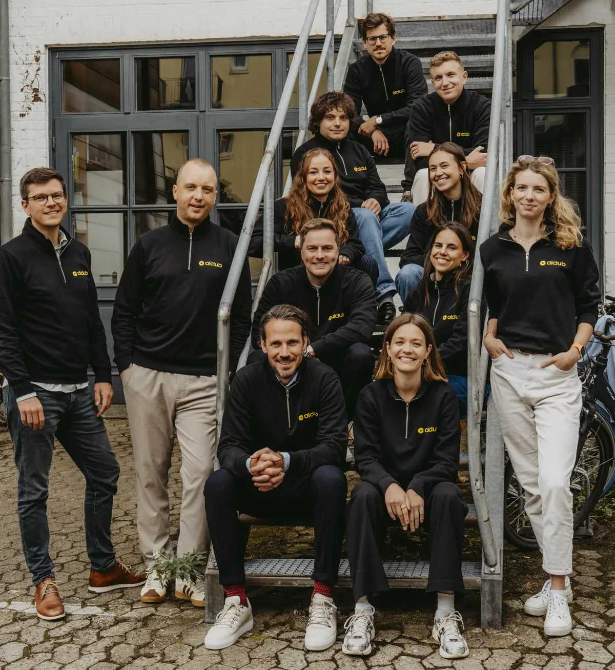 Das Team des AI Club auf einer Außentreppe, vorne der Bürohund Chapito